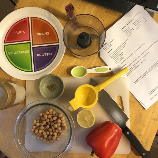 Table top with kitchen items including a cutting board, kitchen knife, recipe, bowl of beans lime and juicer and a plate showing recommended portion sizes.
